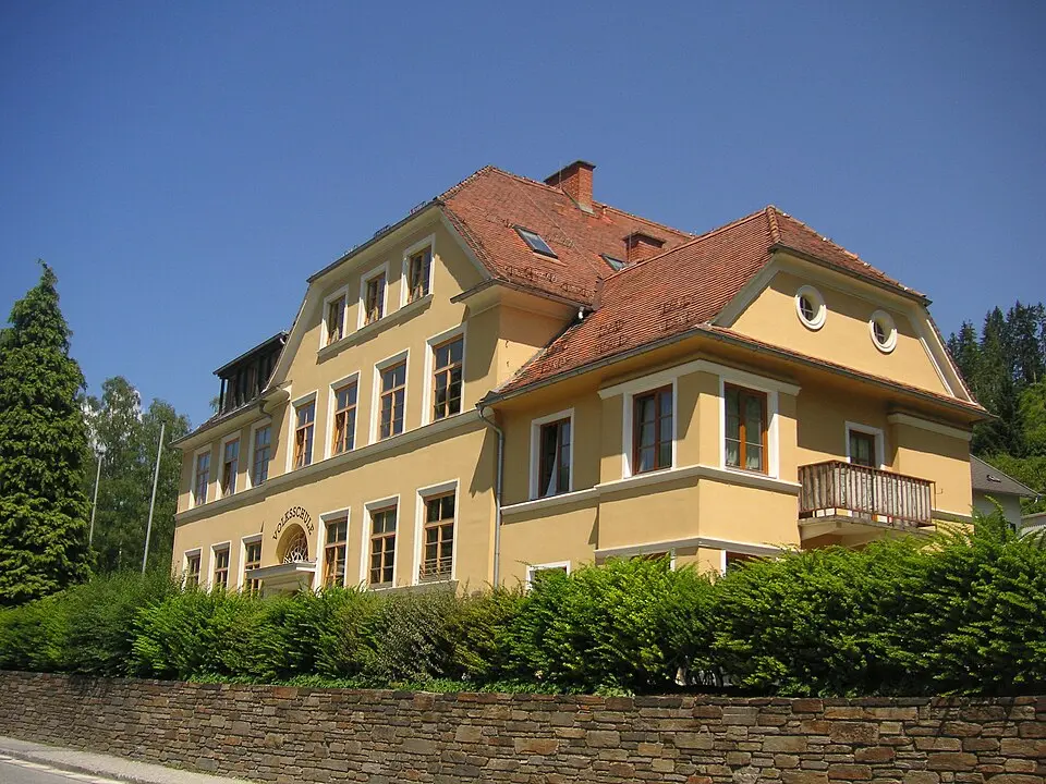 Volksschule Übelbach mit straßenseitiger Mauer und Bildstock